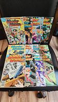 Lot of 12 Wonder Woman comic books arranged on a chair, showing colorful covers with action scenes and various cover designs from the 1970s and 1980s.