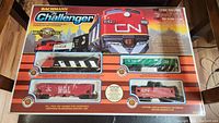 Front view of sealed Bachmann The Challenger train set showing diesel locomotive and three freight cars in original packaging with city skyline background.