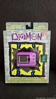 Front of sealed Digimon electronic game package showing purple handheld device and Digimon logo.