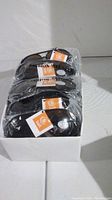 Box containing several individually wrapped black framed sunglasses with orange and white bali tags visible on each.