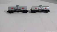 Pair of Mobilgas metal HO scale model train tanker cars on white surface.