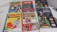 Four vintage comic books with colorful illustrated covers along with two unopened packs of Ultralock comic bags, one pack full and one pack about half full.