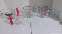 Four measuring cups displayed including two Pyrex glass cups and two OXO plastic cups with red accents.