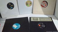 Photo shows five vinyl records in white and black sleeves, some labels visible.