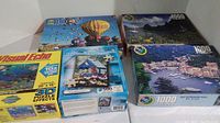 Five boxed jigsaw puzzles shown from front, including Visual Echo, William Vanderdasson, and two 1000-piece landscape puzzles plus one with hot air balloon design.
