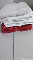 Stack of three white and two pinkish red large bath towels folded and stacked on a surface.