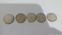 Five worn Canadian silver half dollar coins laid side by side, showing side with Canadian coat of arms.