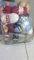 Bag of mixed yarn skeins including colors such as red, white, blue, and beige in a transparent plastic bag.