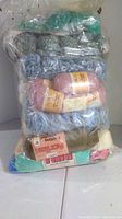 Plastic bag containing multiple skeins of yarn in various colors including green, blue, pink, and beige.