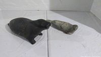 Lot showing two Inuit stone animal carvings, a dark walrus and a lighter seal, placed on white cloth background.