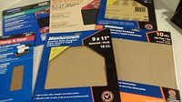 Photo showing several packs of Mastercraft aluminum oxide sandpaper sheets and a sanding clamp block packaged in blue and yellow Mastercraft branded packaging.