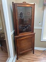 Front view of the dark wood corner curio cabinet with glass door and bottom panel door, showing three shelves inside the glass door section.