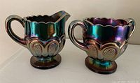 Photo showing both cream pitcher and sugar bowl with iridescent carnival glass finish and embossed details