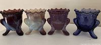 Front view of four Degenhart glass toothpick holders showing their color and leg designs.