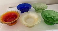 Top view of five vintage glass salt cellars in various colors arranged in a row showing the Star & Dewdrop raised geometric pattern and flared scalloped rims.