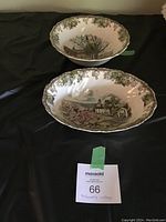 Two Friendly Village bowls shown on black cloth. One round bowl on top and one oval bowl on bottom, both featuring detailed village scenes with floral vine borders.