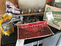 Wrench set, jars, yardsticks, sweeping compound, mortar mix bag arranged on a garage shelf