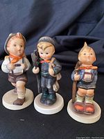 Front view of three Hummel porcelain figurines: School Boy, Chimney Sweep, Little Hiker.