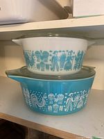 Two Pyrex glass casseroles stacked, showing Amish Butterprint design in blue and white.