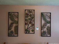 Three metal art panels mounted on a wall showing leaf and flower designs