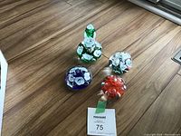 Four vintage Joe St Clair paperweights on wooden floor: three round with florals and one shaped like a perfume bottle with floral details.