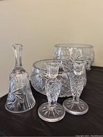 Overall view showing two large cut crystal serving bowls, pair of crystal candle sticks and a crystal bell with pinwheel pattern, placed on black surface.