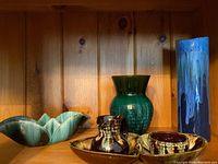 Shelved pottery collection showing various items: green vase, tall blue vase, cream and sugar pots, and bowls.