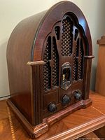Front view of wooden cathedral style radio with decorative grille and trim. Shows control knobs and tuning dial.