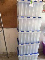Stack of 5 clear plastic totes with blue lids seen from side, showing the totes stacked vertically.
