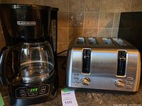 Photo showing both Masterchef four-slice stainless steel toaster and Black & Decker black plastic coffee maker side by side on countertop.