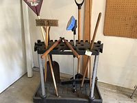 Full view of the plastic tool organizer with various garden tools inserted in slots including broom, shovel, rake, brushes and pruner.