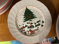Close up of a dessert plate showing Christmas tree, village scene, sleigh and horses, with gold star details