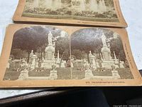 Closeup photo showing stereoview card of cemetery scene with statue and monuments, card on orange-tinted stock with two side-by-side black and white photos