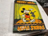 Front cover of Mickey Mouse Illustrated Movie Stories book showing Mickey Mouse on stage with shadow puppet against yellow backdrop and green curtain.