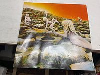 Front cover of Led Zeppelin Houses Of The Holy vinyl record album showing naked children climbing rock formations against an orange sky.