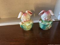 Front view of two ceramic bunnies in cabbage shaped salt and pepper shakers, showing painted facial details and closed eyes.