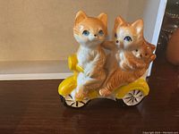 Front view of the ceramic salt and pepper shakers shaped as two cats on a yellow motorcycle, showing details of the cats and small kitten held.