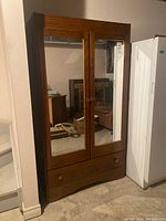 Front view of wooden Canadian armoire with mirrored double doors and lower drawer, showing overall size and design.