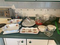Photo showing a variety of kitchenware on a counter including porcelain serving dishes, Pyrex measuring cup, glass pitcher, glass bowls, and dishes.