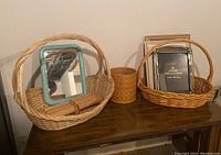 Woven baskets including a large basket with handles, a small hinged basket, a small woven cylindrical container, a blue framed mirror, and several photo frames.