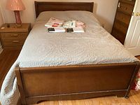 Full view of wooden bed frame showing footboard and bedding, with packaged linens on top