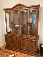 Front angle photo of decorative wooden buffet with four upper glass doors and shelves, four lower carved wooden doors