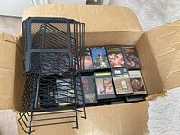 Open cardboard box filled with assorted cassette tapes and three black metal file holders stacked on top.
