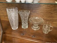 Four pieces of decorative glass: two vases, one pitcher, one fruit bowl set on a wooden surface
