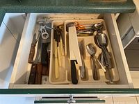 Drawer showing various kitchen utensils including knives, can opener, and cutlery in plastic tray organizer