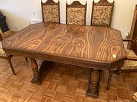 Front angled view showing the wooden table top with prominent wood grain, slight scratches, and three chairs with floral upholstery behind.