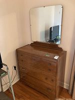 Front view of the wood dresser with mirror, showing three drawers with different handles and scratches on the finish.