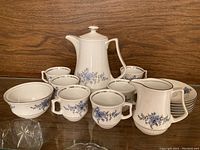 Full view of the espresso set showing the tall pot, creamer, sugar bowl, six cups, and saucers arranged on a wood surface.