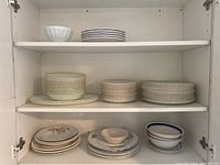 Shelves holding a variety of stacked Fire King dishes including bowls, dinner plates, salad plates and serving platters in white and floral patterns.