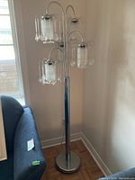 Full view of the decorative metal floor lamp near a couch and window, showing its height and base.